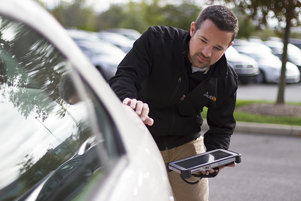 Image of a man leaning and examining a car while holding a tablet device